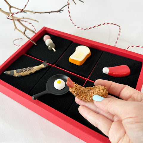 6 utensil rests in a red box with black padding. One being held by a woman's hand.